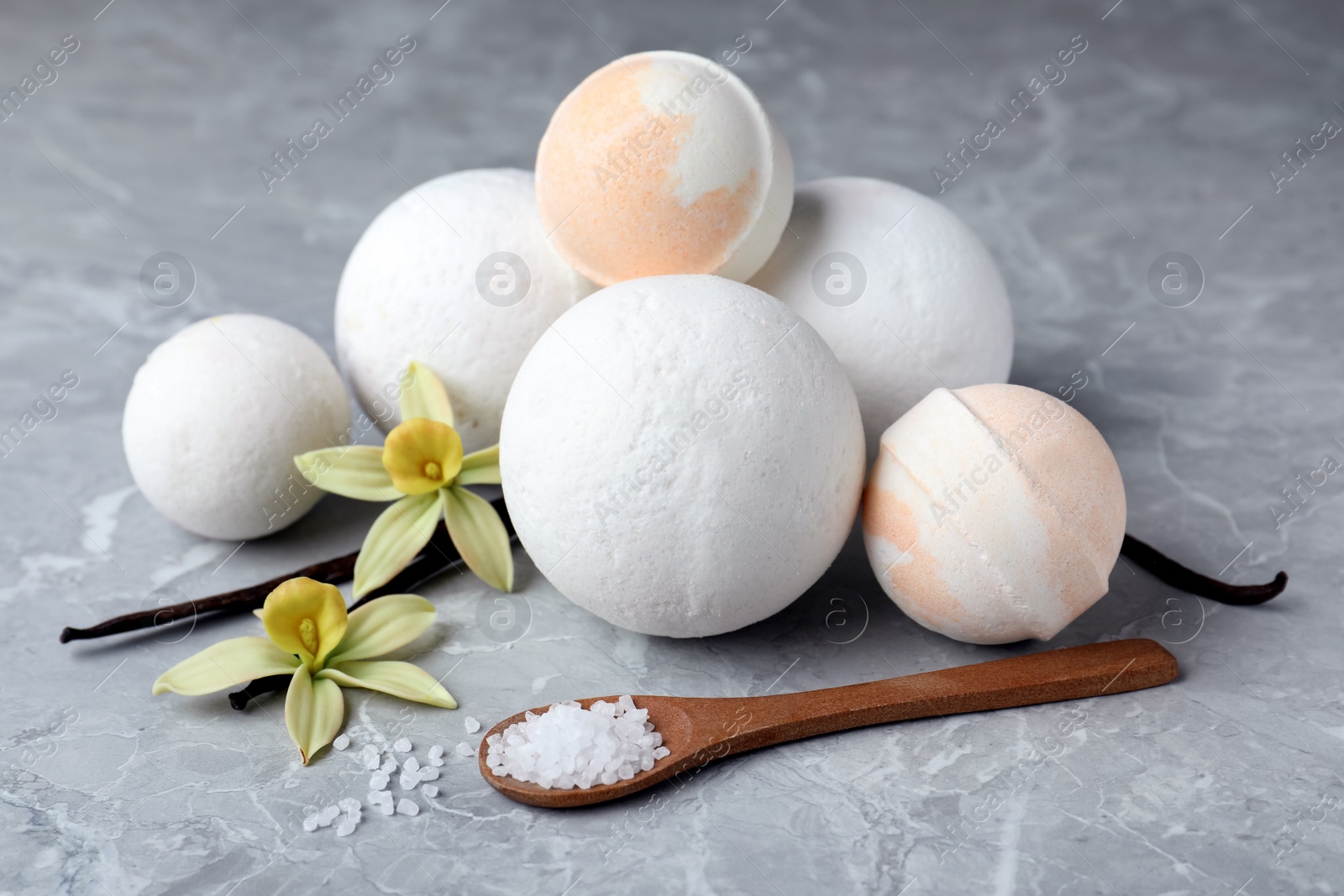 Photo of Fragrant bath bombs, sea salt, vanilla sticks and flowers on grey marble table