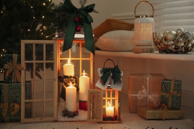 Wooden decorative lanterns with burning candles near Christmas tree in room