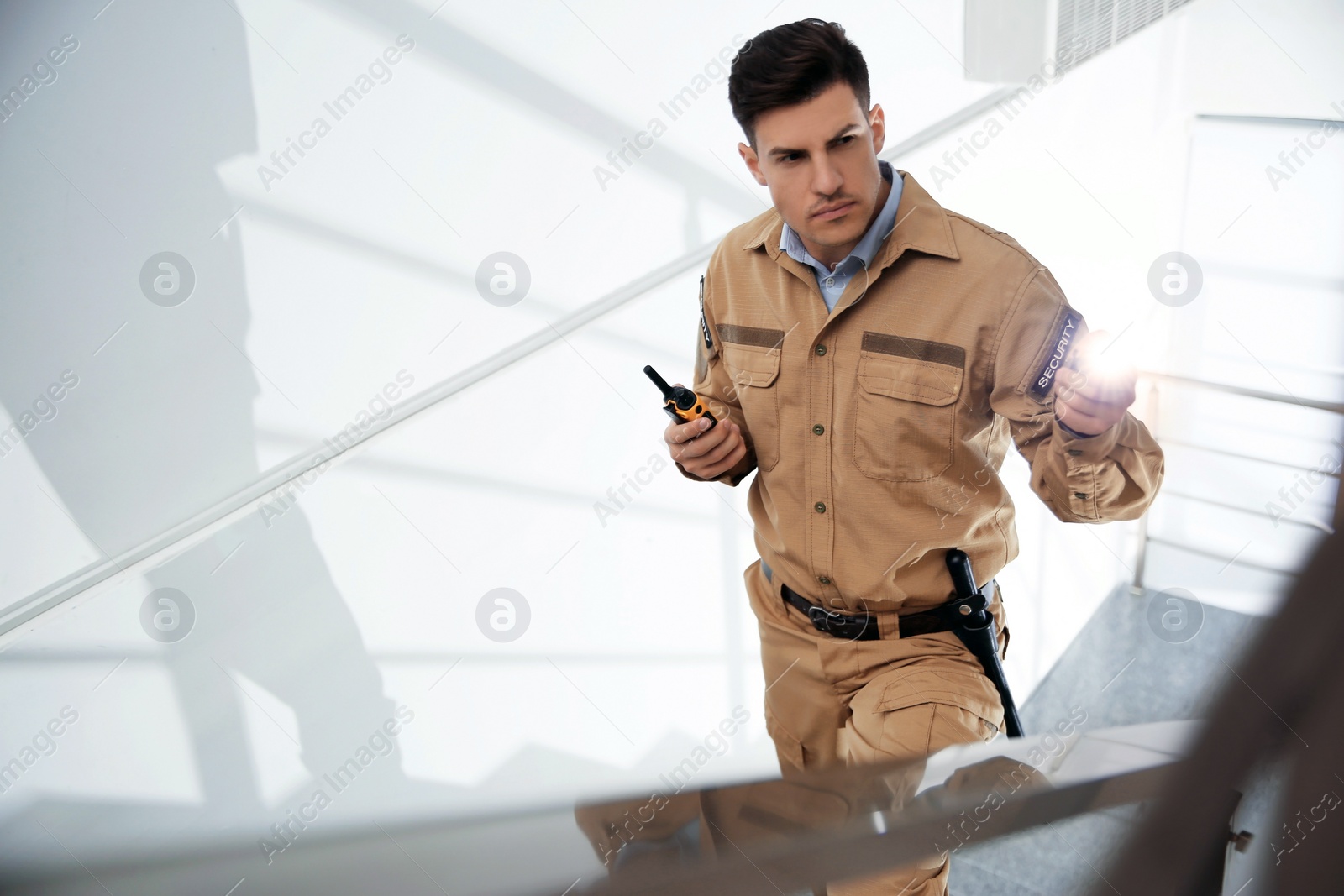 Photo of Professional security guard with portable radio set and flashlight on stairs