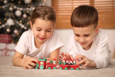 Photo of Cute little children playing with colorful train toy in room decorated for Christmas