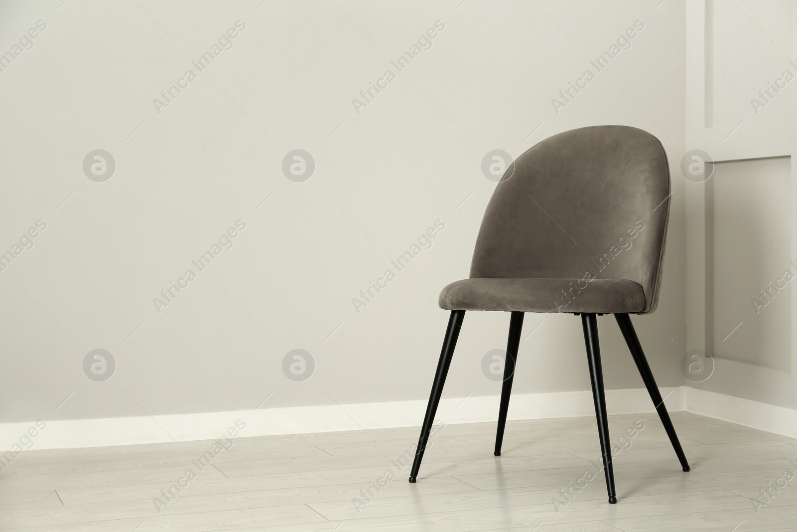 Photo of Stylish grey chair near light wall in room. Space for text