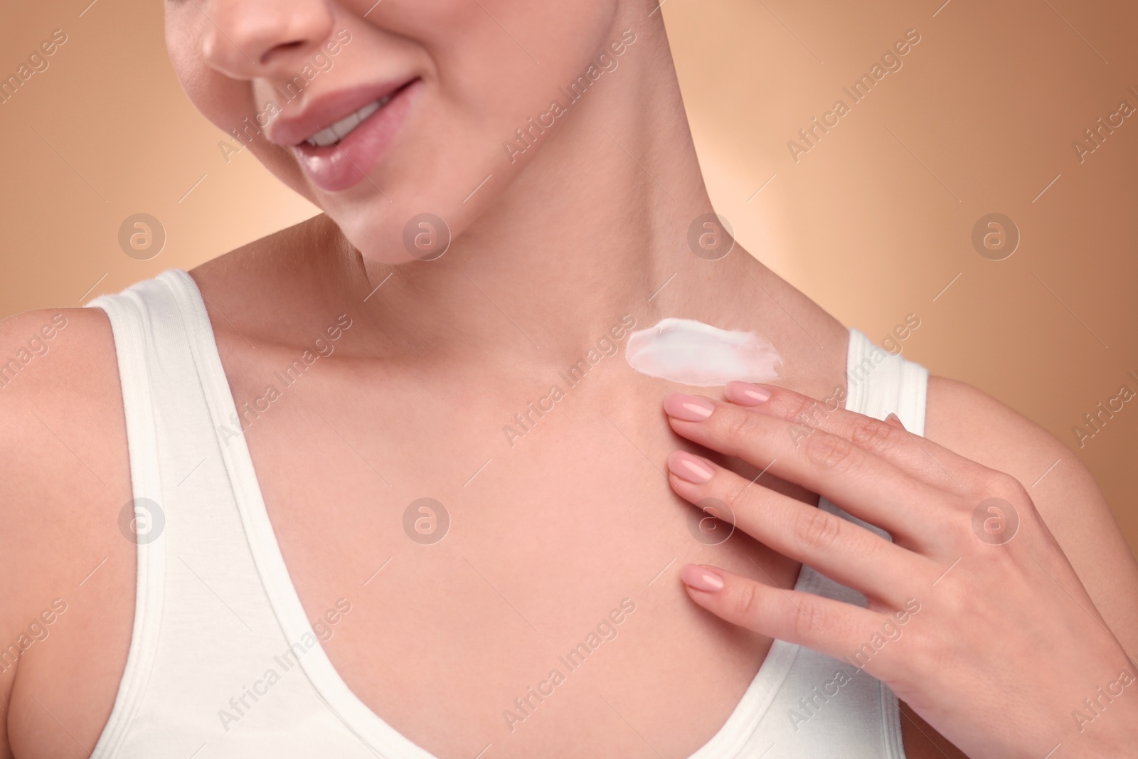 Photo of Woman with smear of body cream on her neck against light brown background, closeup