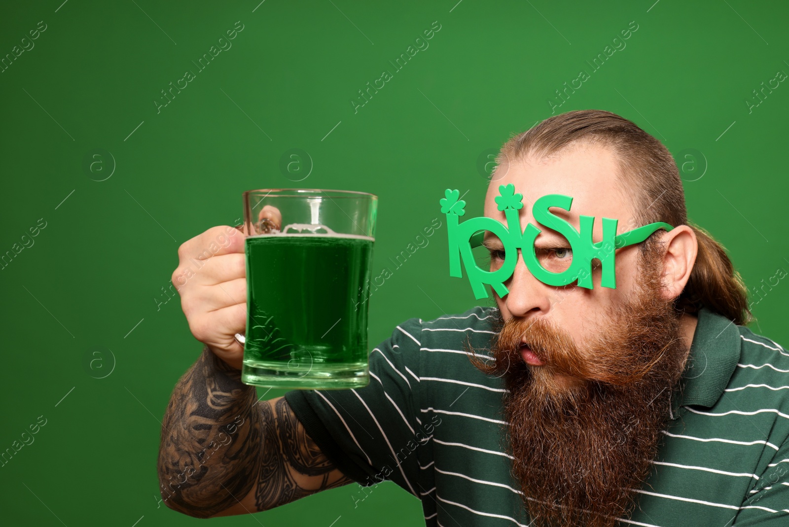 Photo of Bearded man in party glasses with green beer on color background. St. Patrick's Day celebration