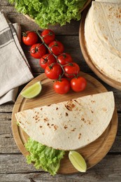 Tasty homemade tortillas, tomatoes, lime and lettuce on wooden table