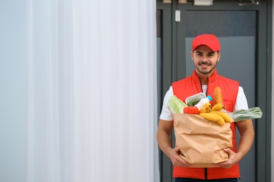 Food delivery courier holding paper bag with groceries indoors. Space for text