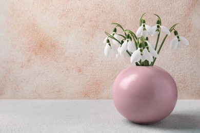Photo of Beautiful snowdrops in vase on white wooden table, space for text