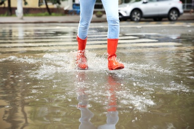 Photo of Woman with red rubber boots running in puddle, closeup. Rainy weather