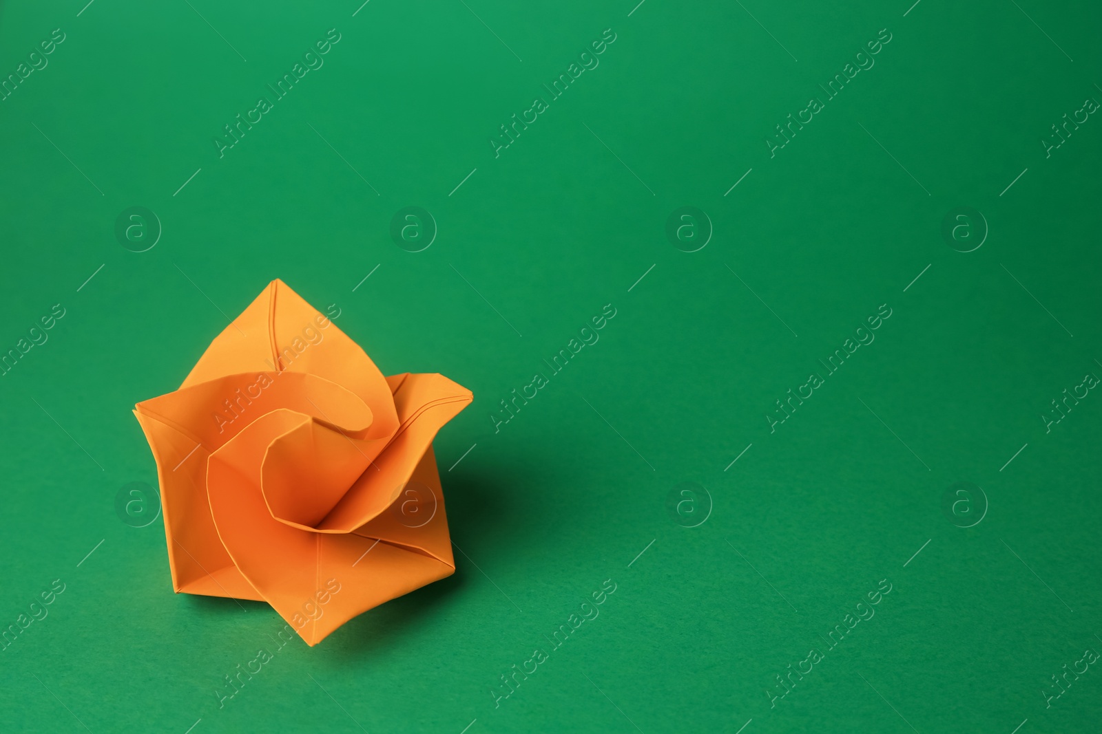 Photo of Origami art. Handmade orange paper flower on green background, space for text