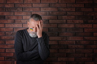 Sad senior man with picture of Ukrainian flag on cheek near brick wall, space for text. Stop war in Ukraine