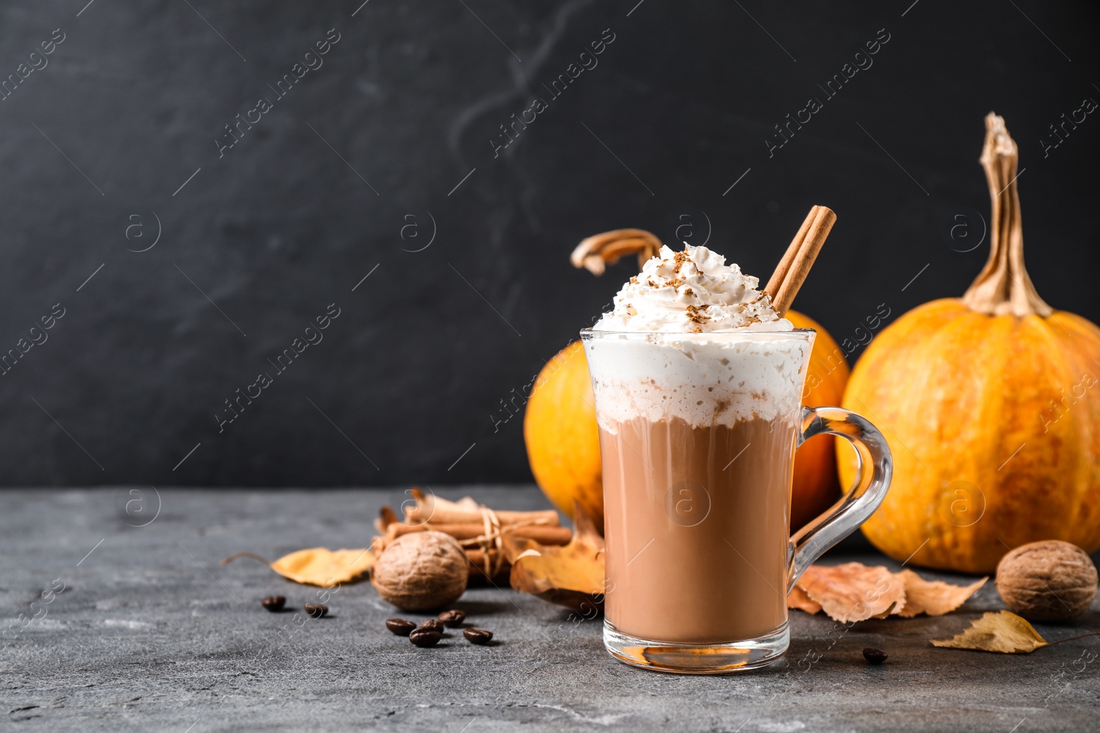 Photo of Pumpkin spice latte with whipped cream and cinnamon stick in glass cup on grey table. Space for text