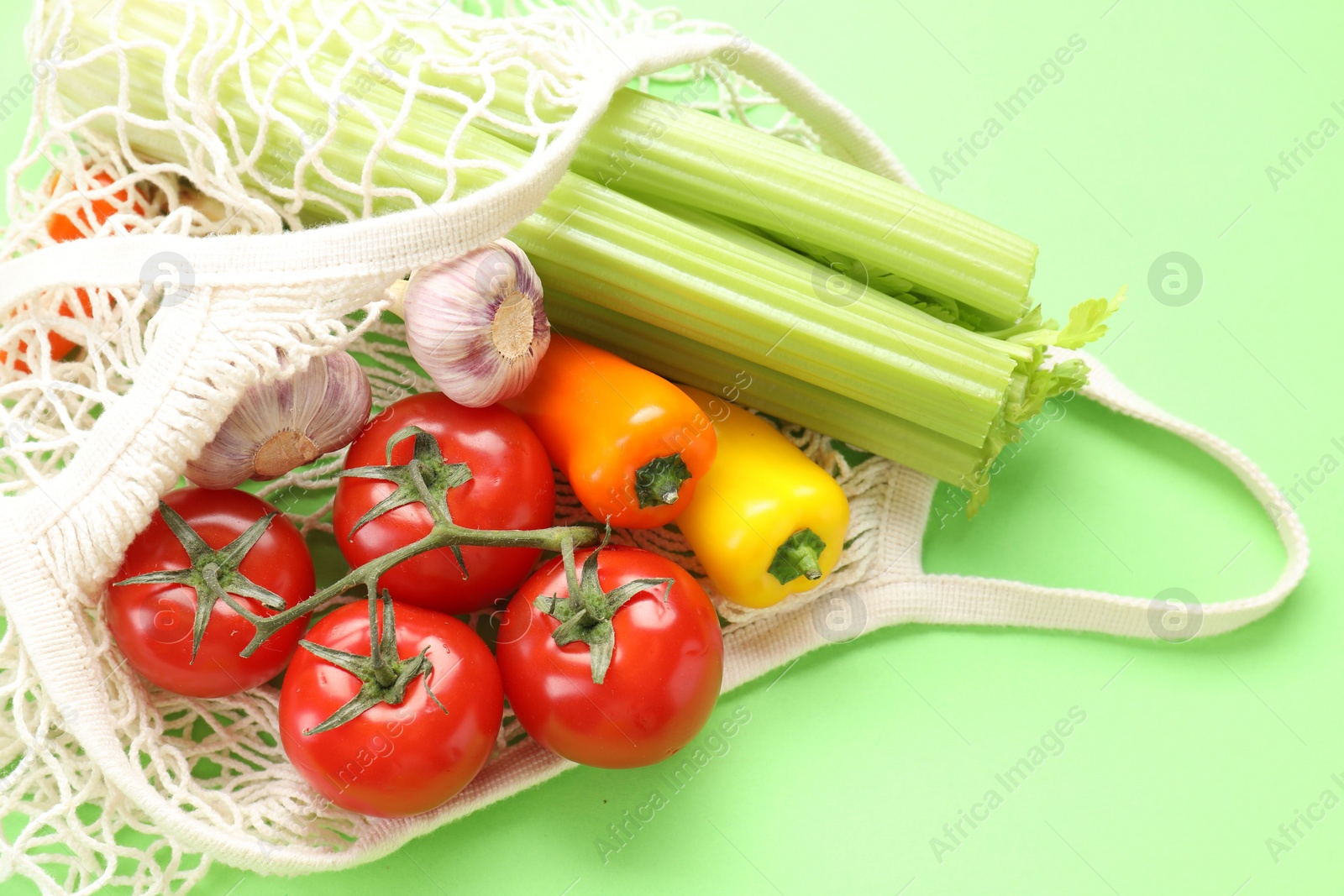 Photo of String bag with different vegetables on light green background, closeup