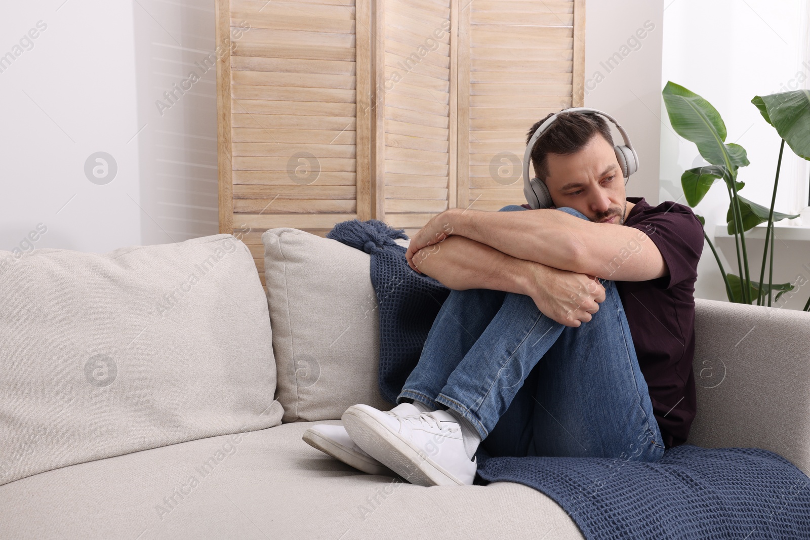 Photo of Upset man listening to music through headphones on sofa at home. Loneliness concept