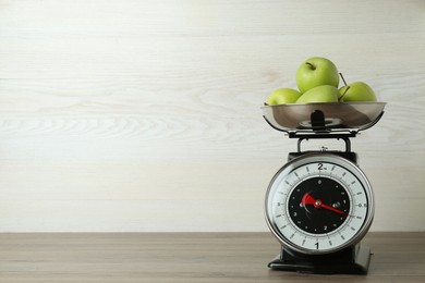 Photo of Kitchen scale with green apples on wooden table. Space for text