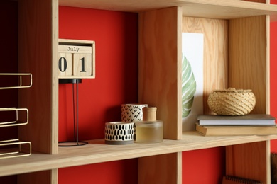 Stylish wooden shelf with decorative elements on red wall