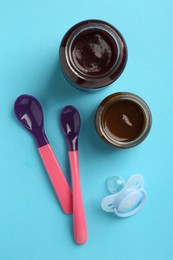 Photo of Jars with healthy baby food, spoons and pacifier on light blue background, flat lay