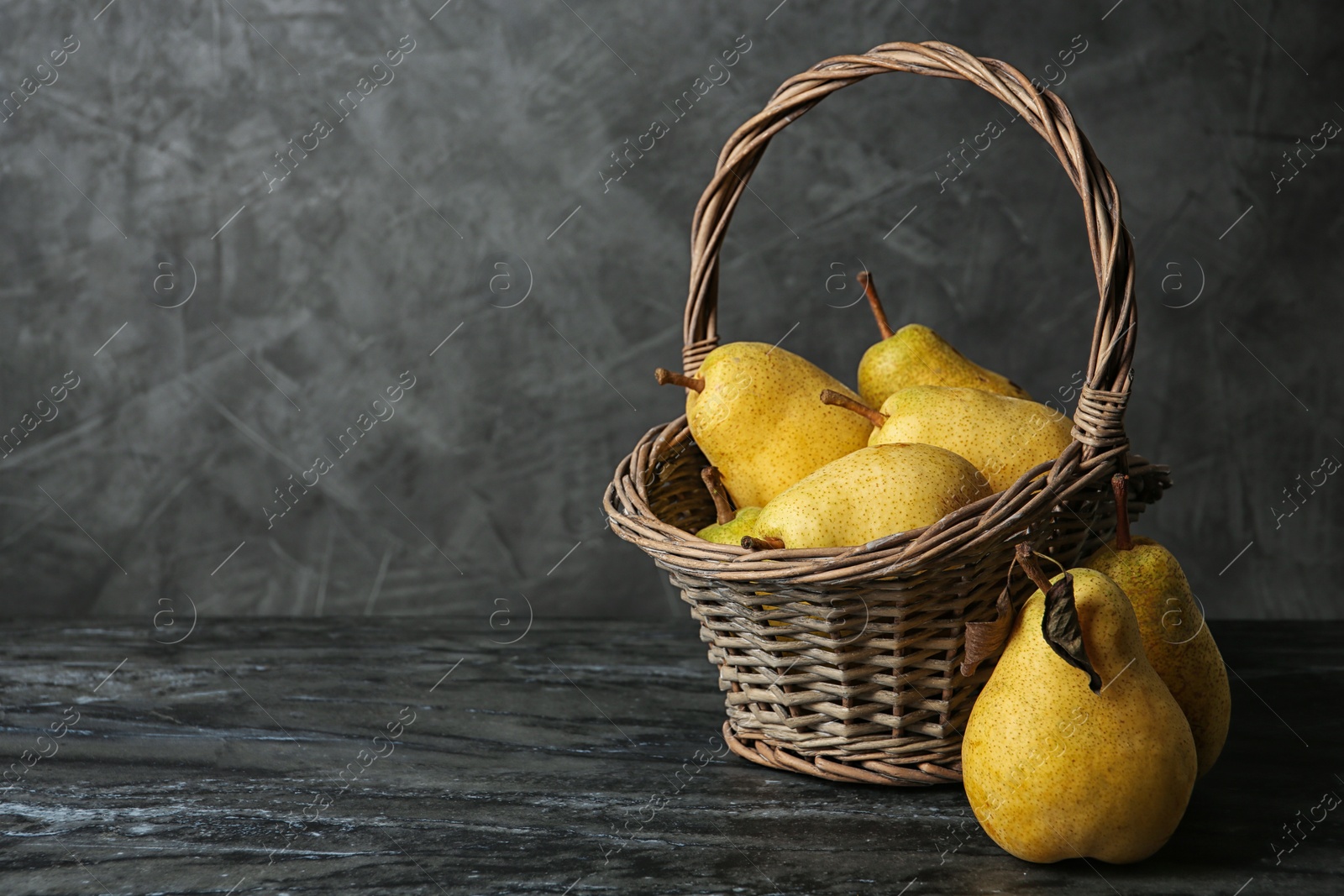 Photo of Basket of fresh ripe pears on table against gray background with space for text