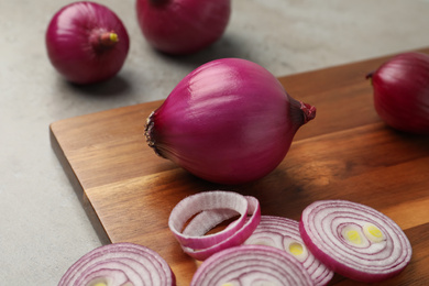 Photo of Red onion and wooden board on light grey table, closeup