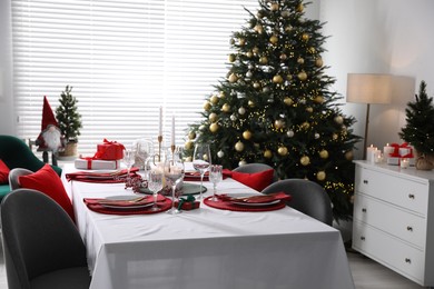 Christmas table setting with burning candles, gift box and dishware in room