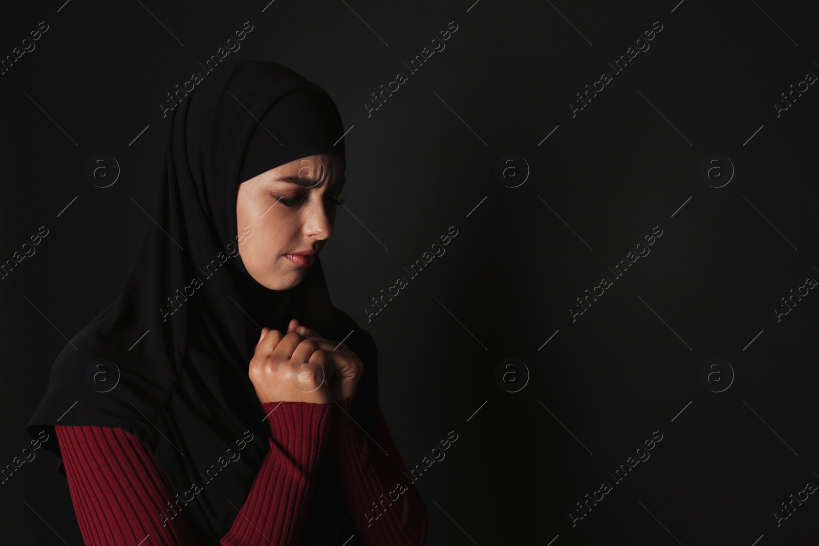 Photo of Portrait of sad Muslim woman in hijab  praying on dark background. Space for text