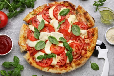 Photo of Delicious Caprese pizza with tomatoes, mozzarella and basil on light grey table, flat lay