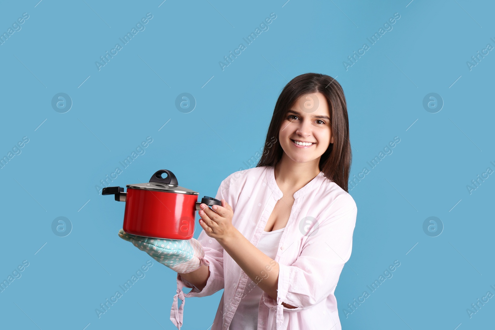 Photo of Happy young woman with cooking pot on light blue background