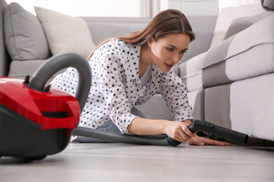 Photo of Young woman using vacuum cleaner at home