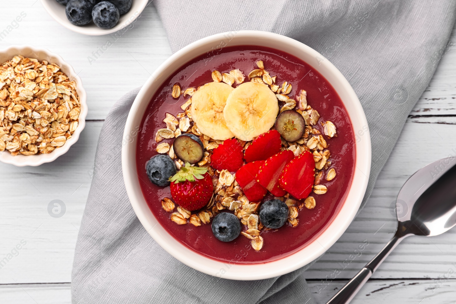 Photo of Delicious smoothie bowl with fresh berries, banana and granola on white wooden table, flat lay