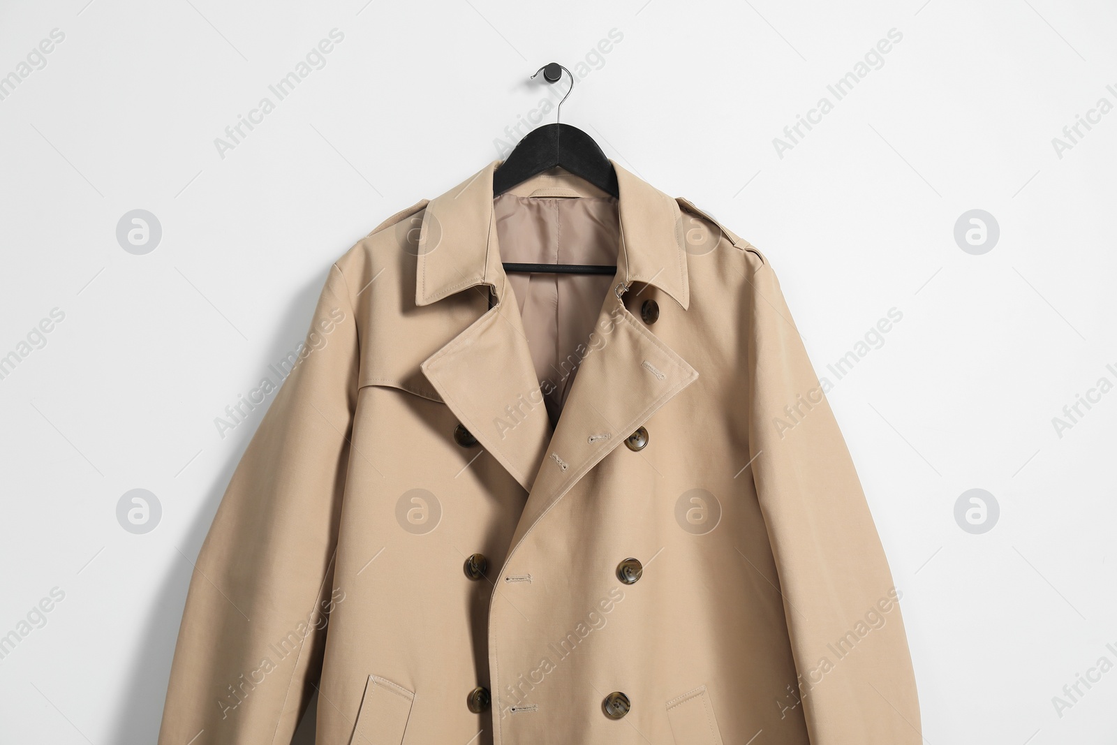 Photo of Hanger with beige trench coat on white wall