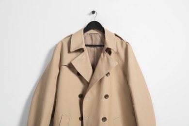 Hanger with beige trench coat on white wall