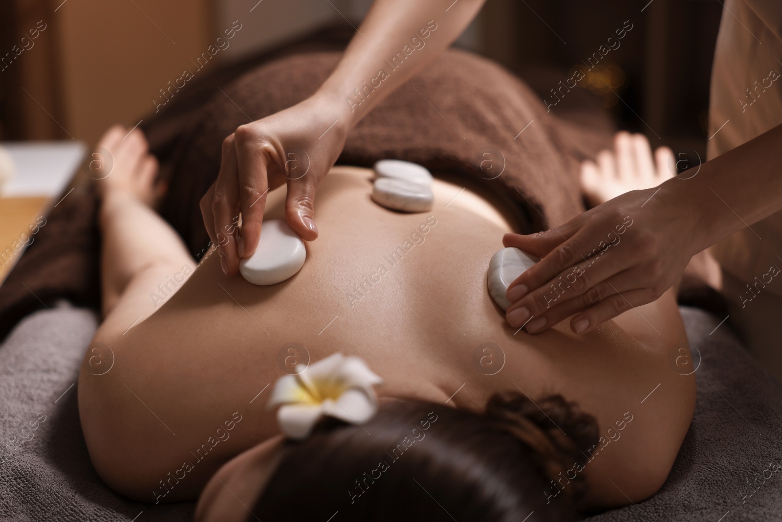 Photo of Spa therapy. Beautiful young woman lying on table during hot stone massage in salon, closeup