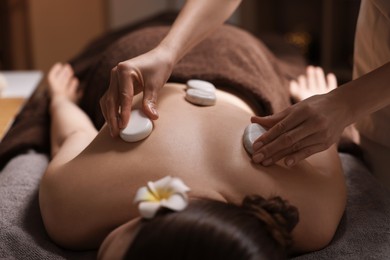 Spa therapy. Beautiful young woman lying on table during hot stone massage in salon, closeup