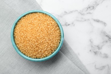 Brown sugar in bowl on white marble table, top view. Space for text