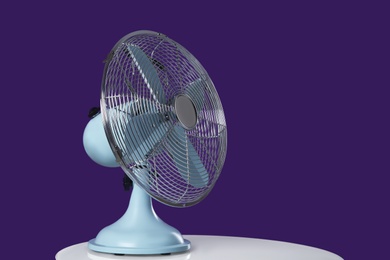 Photo of Modern electric fan on white table against violet background