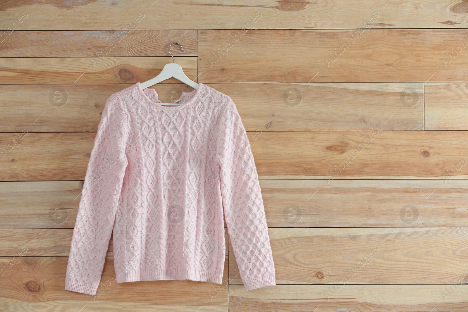 Photo of Hanger with stylish sweater on wooden wall