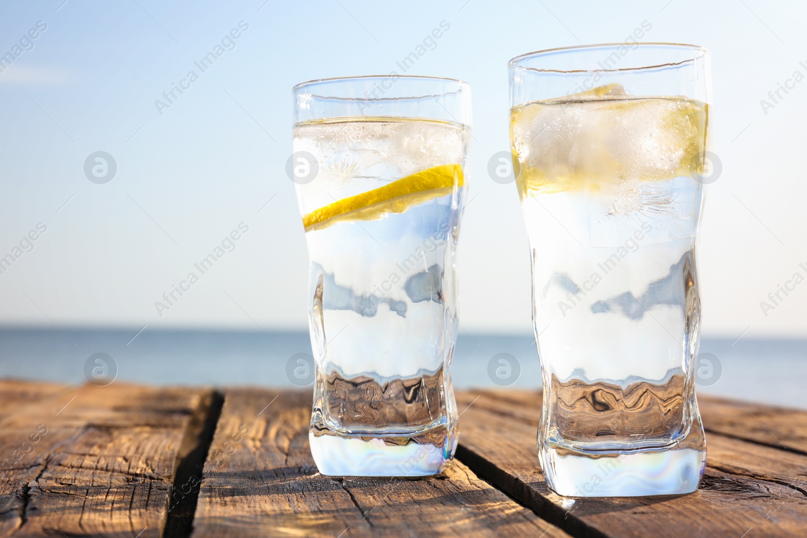 Photo of Wooden table with glasses of refreshing lemon drink on hot summer day outdoors, space for text