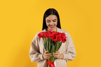 Happy woman with red tulip bouquet on yellow background. 8th of March celebration