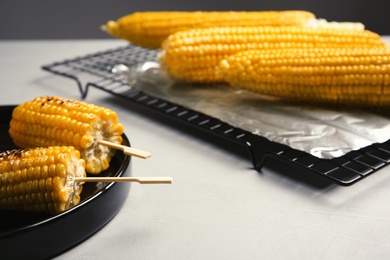 Photo of Ceramic plate with grilled corn cobs on light table