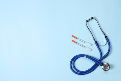 Stethoscope and syringes on light blue background, top view. Space for text