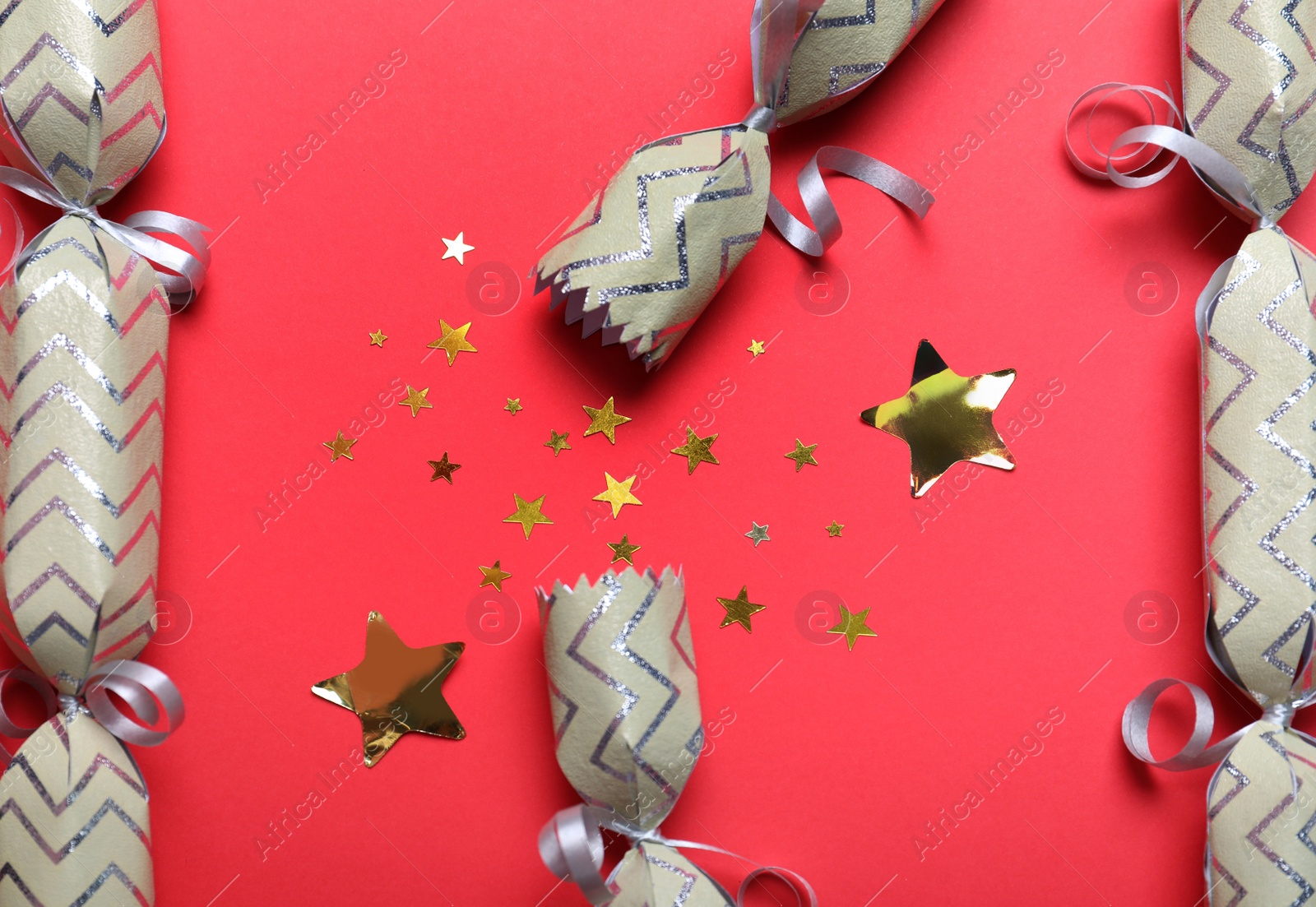 Photo of Open and closed Christmas crackers with shiny confetti on red background, flat lay