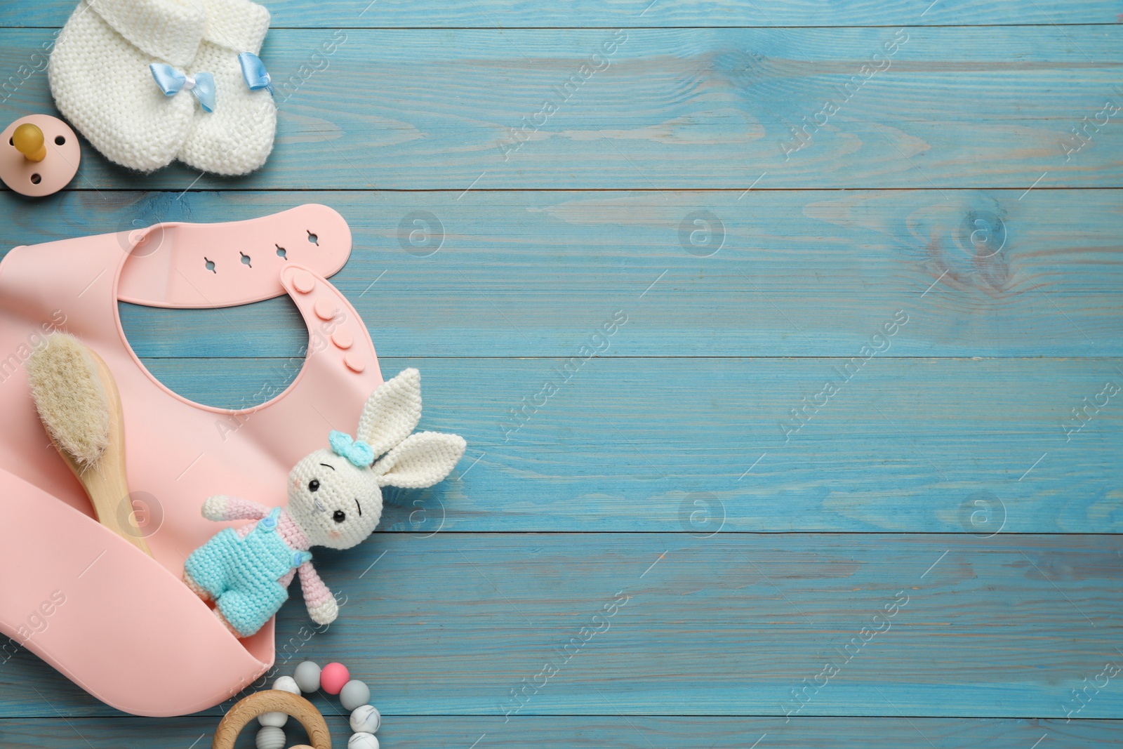 Photo of Flat lay composition with silicone baby bib, toys and accessories on light blue wooden background. Space for text