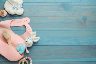 Flat lay composition with silicone baby bib, toys and accessories on light blue wooden background. Space for text