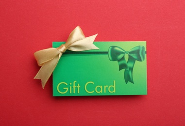 Gift card with bow on red background, top view