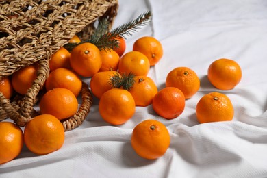 Stylish wicker bag with ripe tangerines on white bedsheet