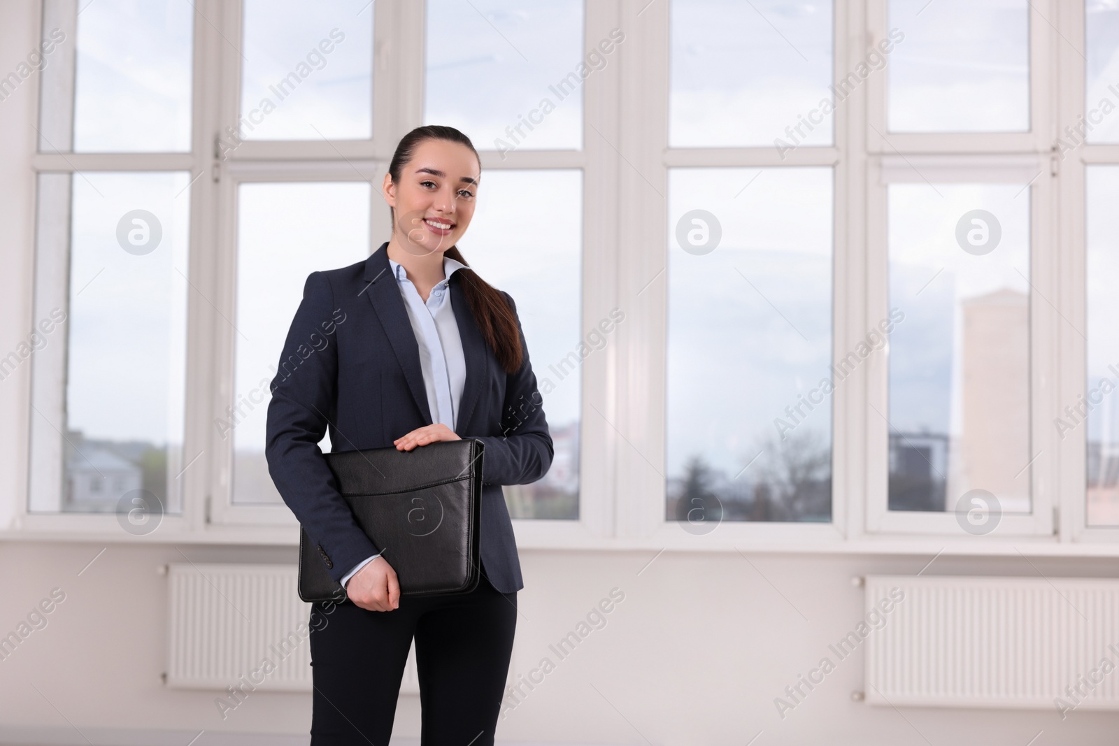 Photo of Happy real estate agent with leather portfolio indoors. Space for text