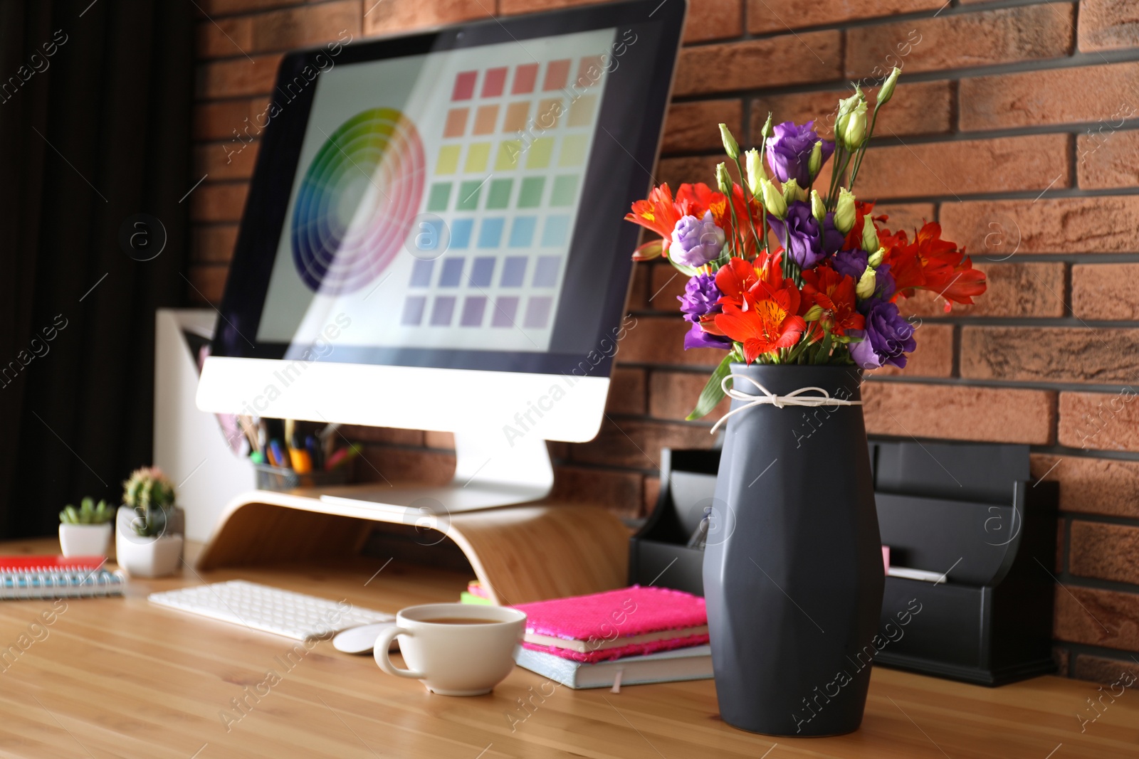 Photo of Stylish vase with fresh flowers and cup on wooden table at workplace