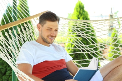 Man with book relaxing in hammock outdoors on warm summer day