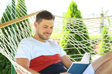 Photo of Man with book relaxing in hammock outdoors on warm summer day