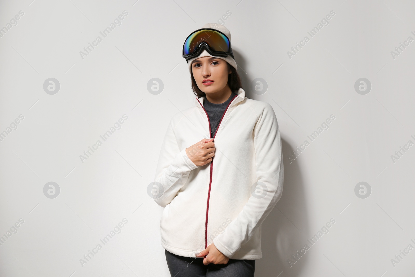 Photo of Woman wearing fleece jacket and goggles on light grey background. Winter sport clothes