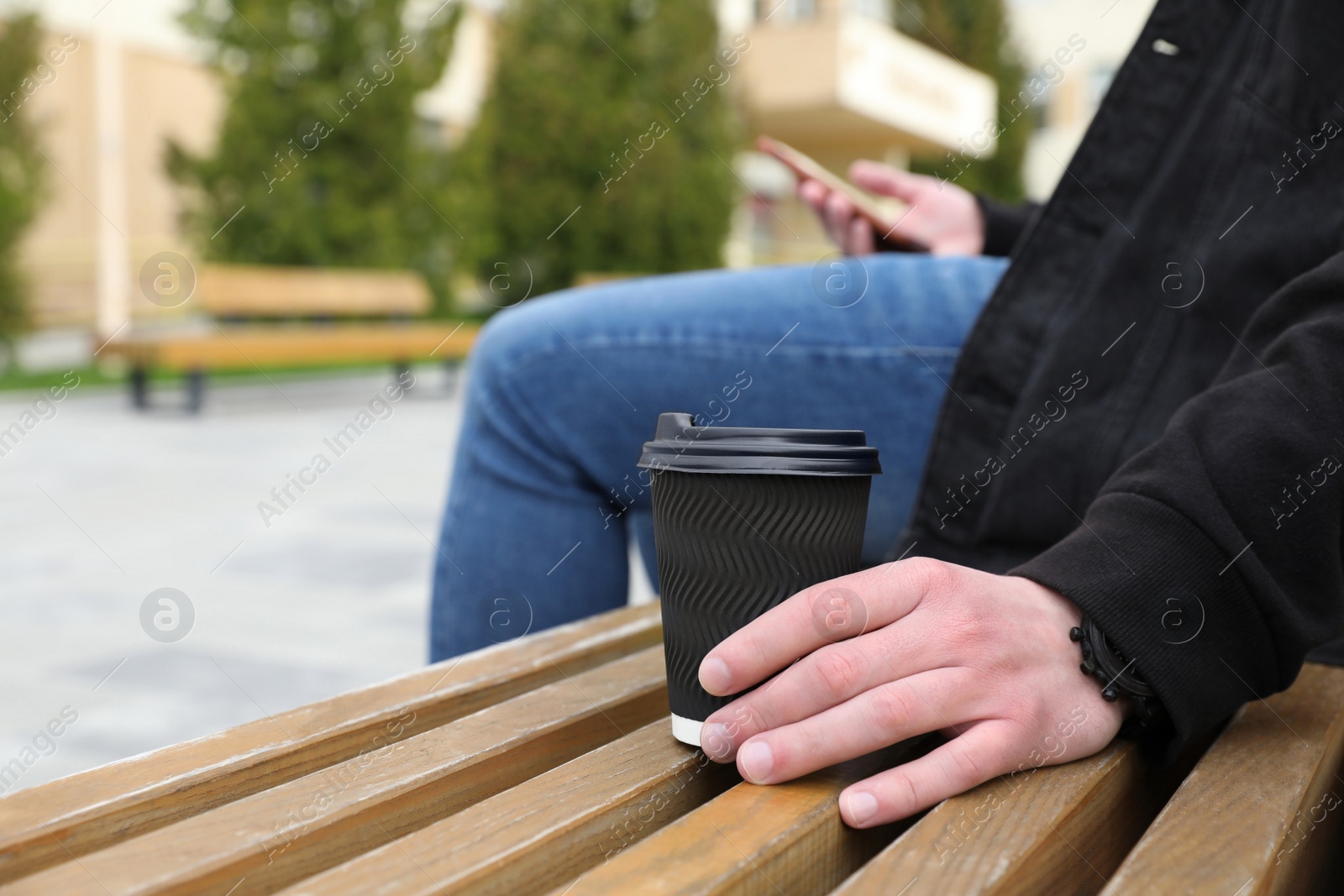 Photo of Man with paper cup of drink on wooden bench outdoors, closeup