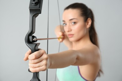 Young woman practicing archery against light grey background, focus on bow